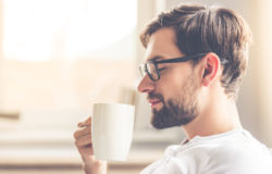 66449949 - handsome man in eyeglasses is smelling the aroma of coffee and smiling while resting at home